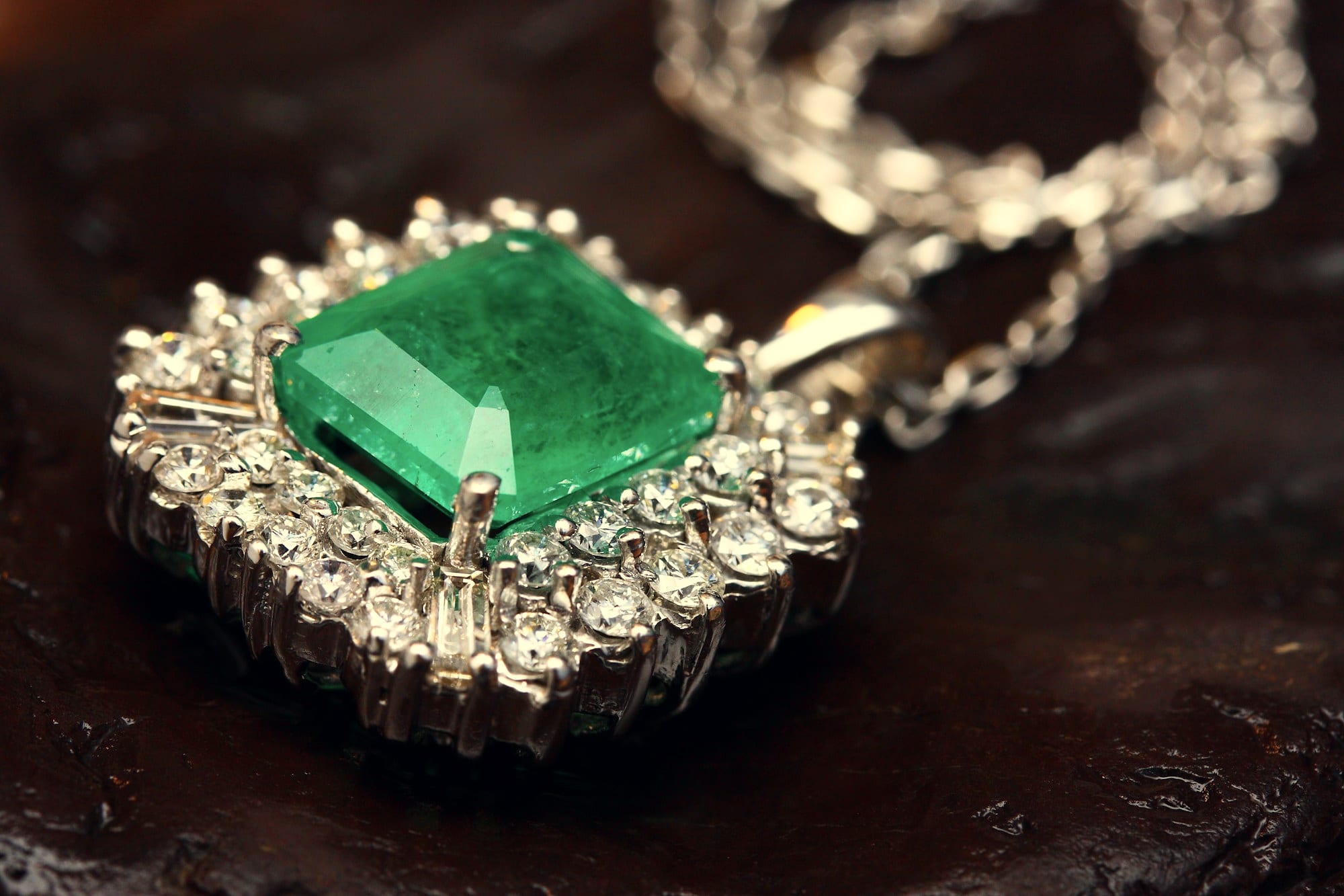 An emerald and diamond pendant on a dark ground, lit from one side.