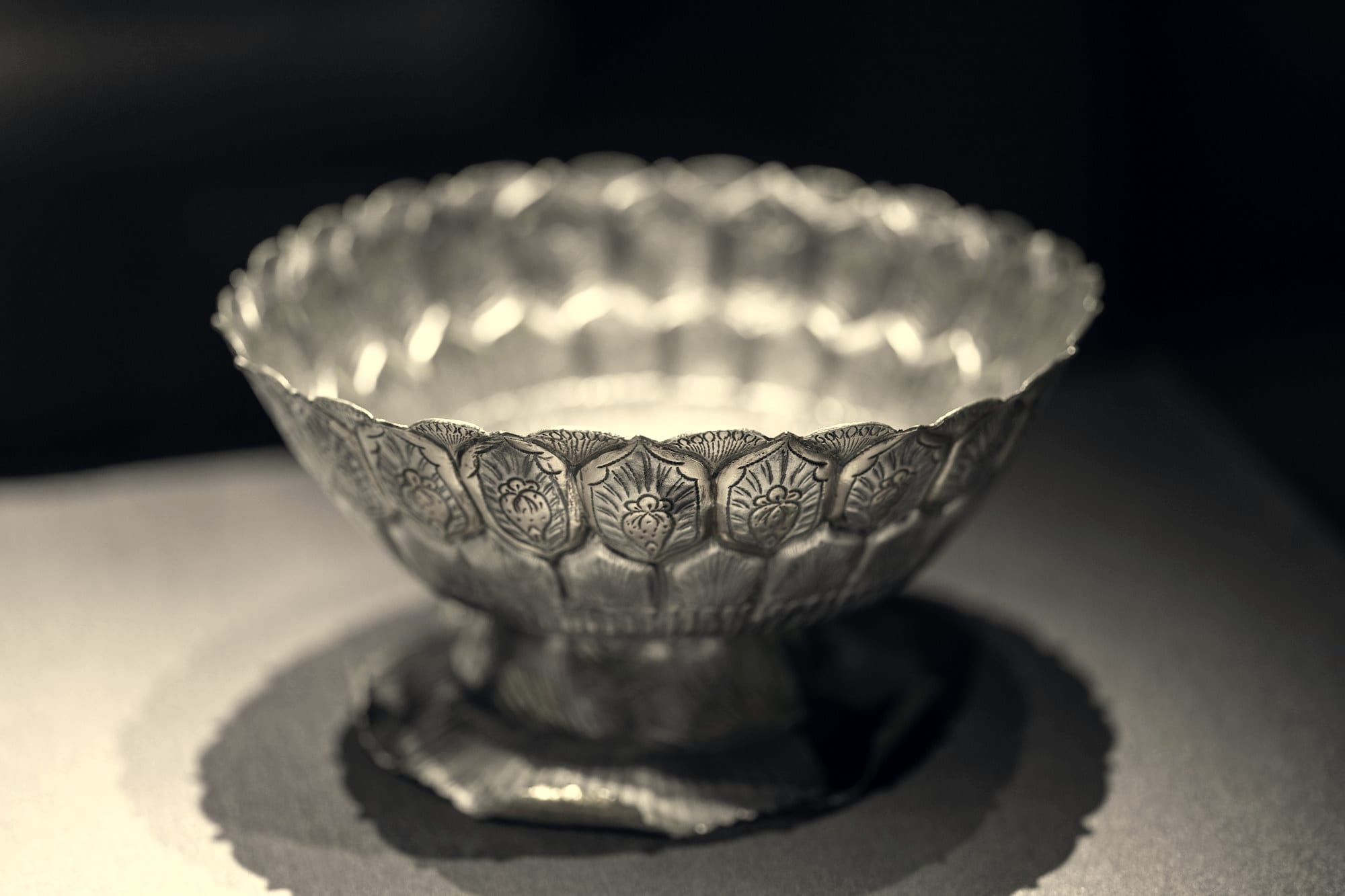 A silver artefact on a dark ground, lit from one side.