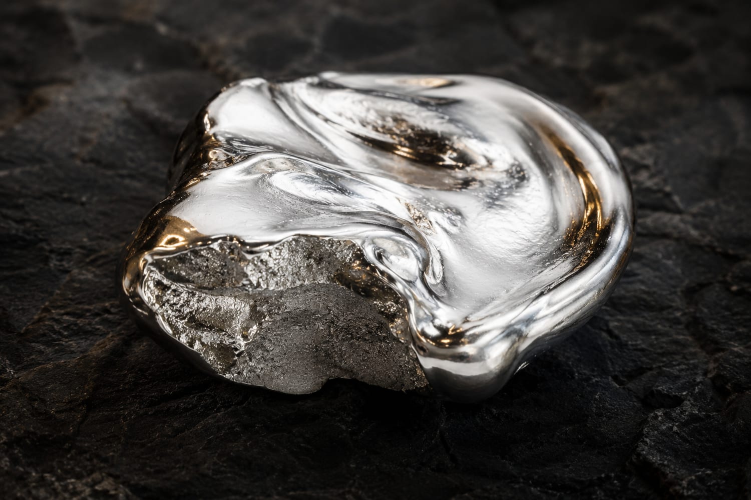 Molten silver caught mid-flow over dark stone, its surface still bright.