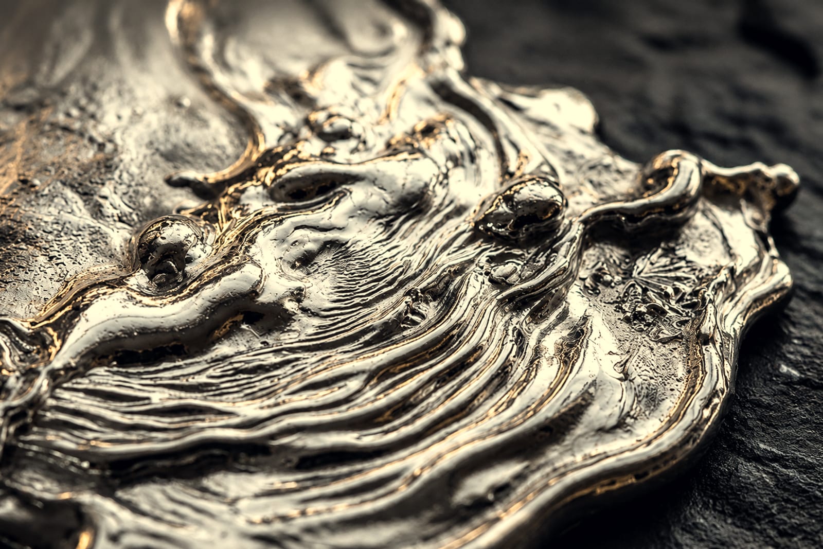 A poured metal surface in macro, its flow lines caught against dark stone.
