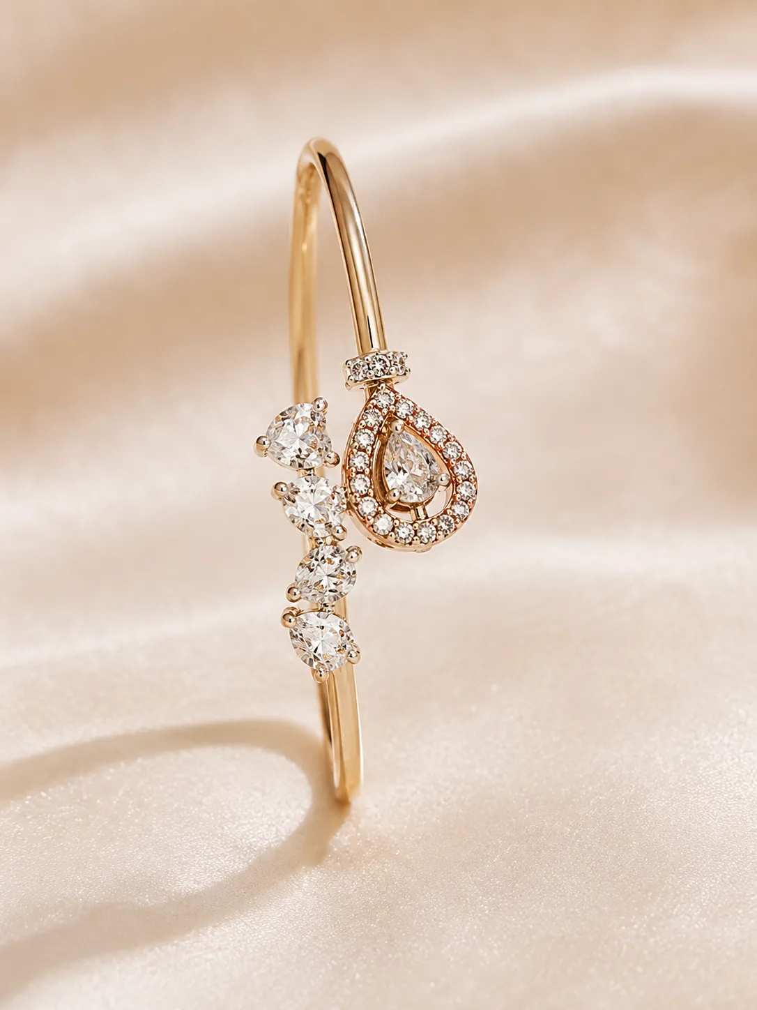 A fine gold-tone open cuff set with a pear-cut colourless stone in a halo and a scatter of smaller colourless stones, on cream satin.