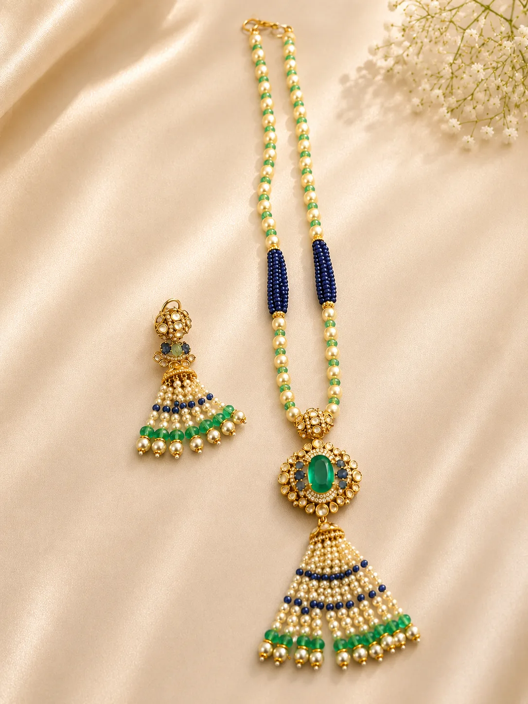 The same beaded necklace and one drop earring arranged on cream satin, with the full length of the strand and its dark blue bead sections visible.