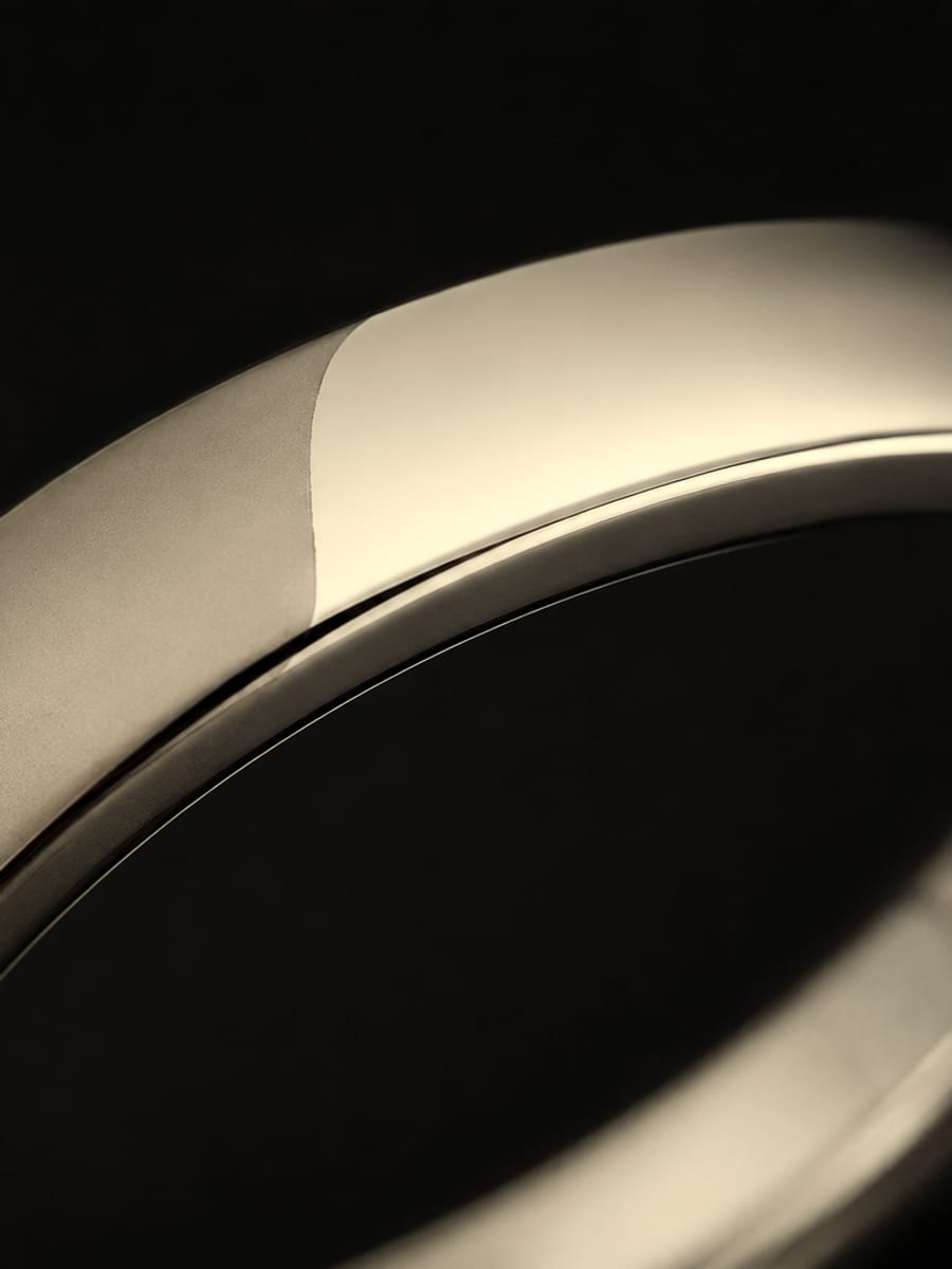 A band ring in macro, one half mirror-polished and one half matte, on black.