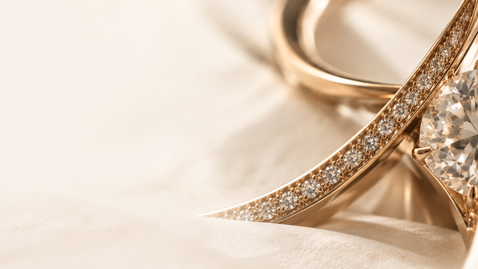 A rose-gold band set with a row of small stones curving past a large faceted gem, on a soft ivory ground.